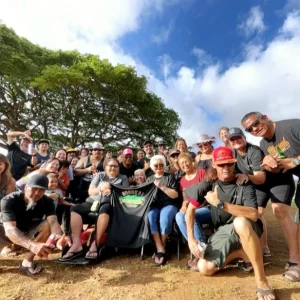 A group of individuals smiling and posing for a photo in front of a large, leafy tree.